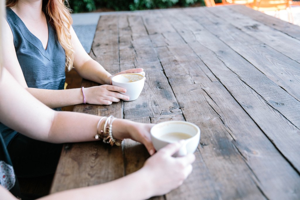 The torsos and arms of two people drinking coffee at a wooden table.