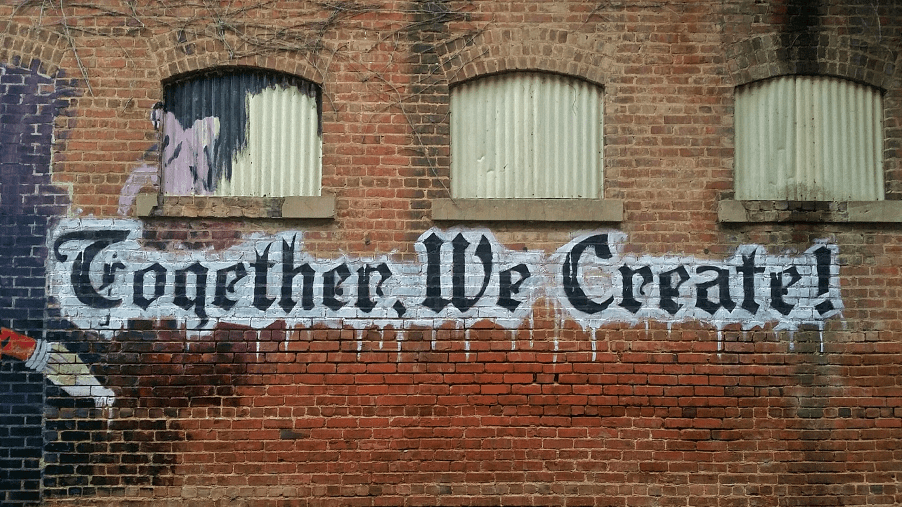 Graffiti on a red brick wall reading  'Together We Create'