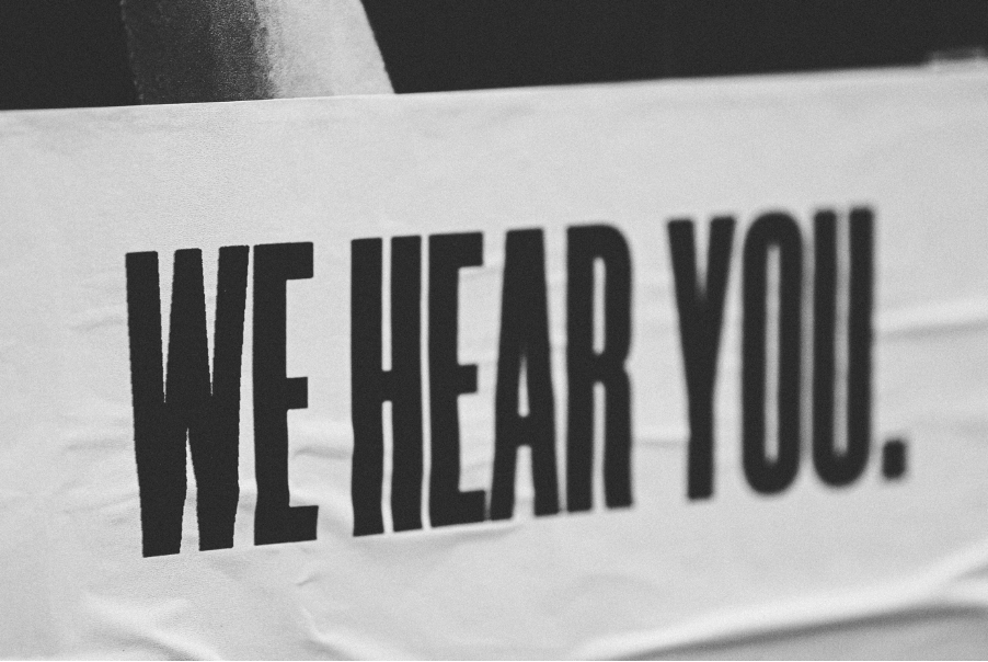 A poster reading 'we hear you' in large black block capital print.