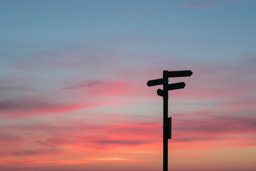 A sunset, showing a silhouetted multi-directional sign post.