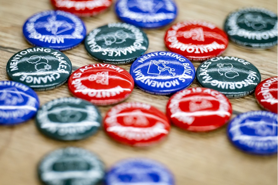 Blue, red and green badges on a table. They have mentoring slogans on them.