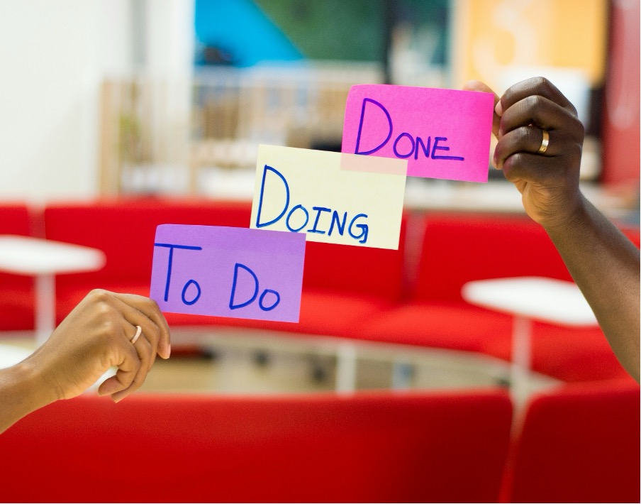 Two hands sticking Post-its on a window. The Post-its read ‘to do’, ‘doing’ and ‘done’.